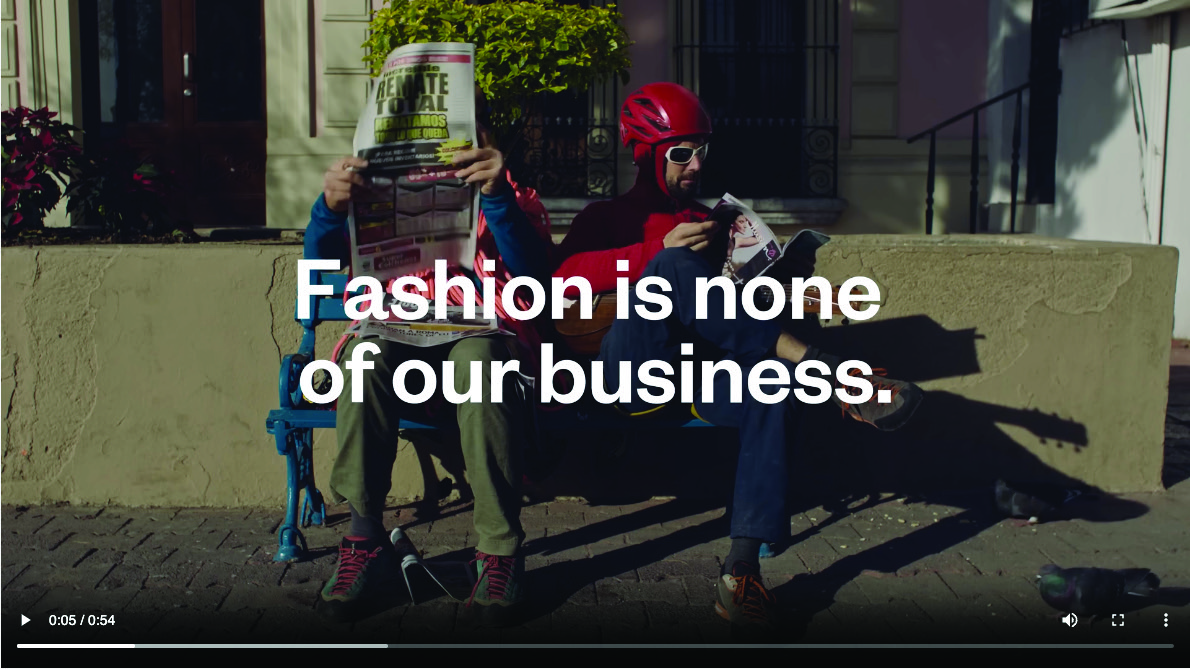 Still from the Unfashionable video ad. Text on top of two people sitting on a park bench reading the newspaper wearing sports kits reads "Fashion is none of our business." 